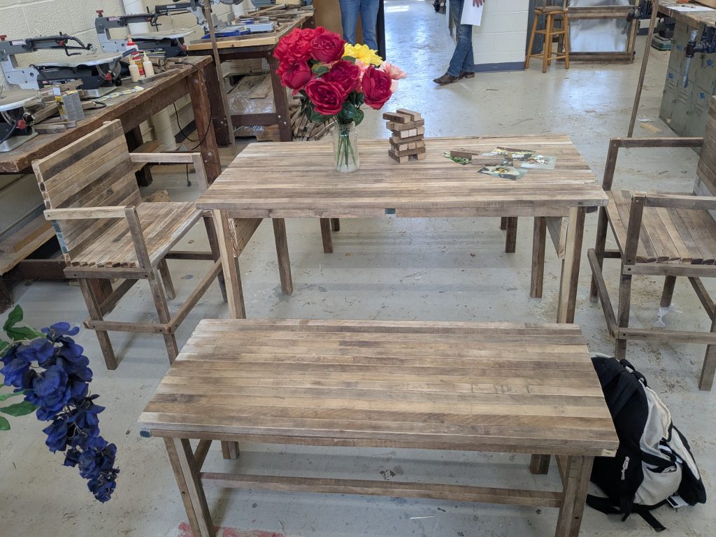 Outdoor dining and sitting set with a table, benches, chairs, flowers, and a small block game made from spacer-stick wood.