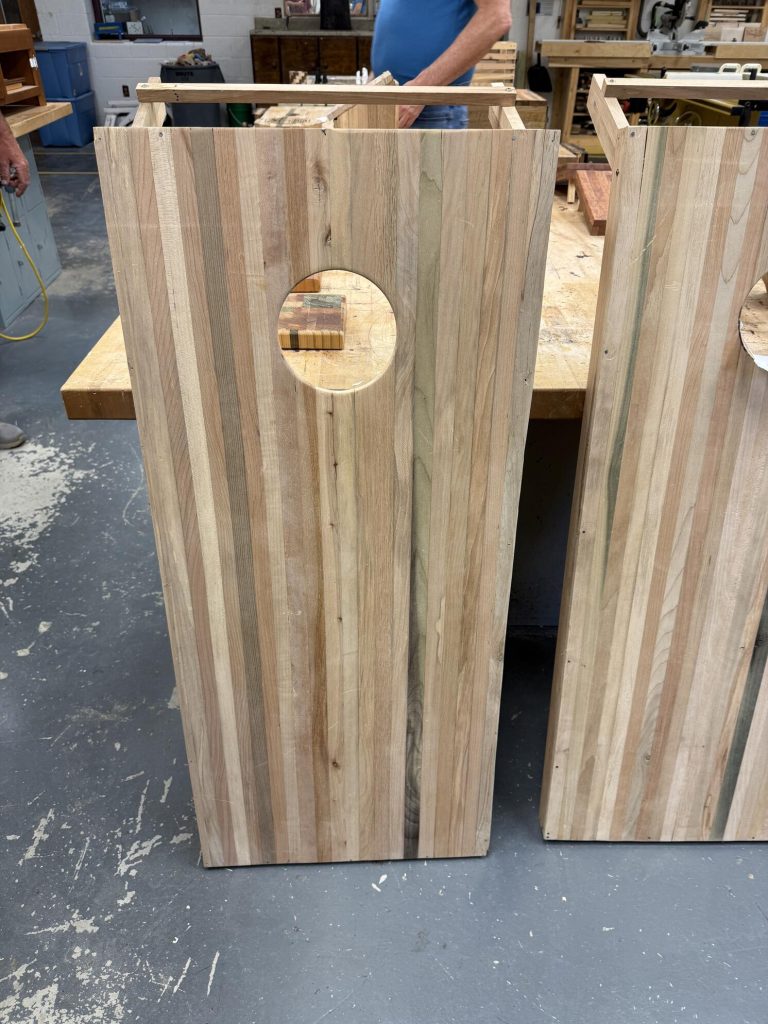 Close-up of a laminated wooden cornhole board with a circular target hole and striped spacer-stick surface.