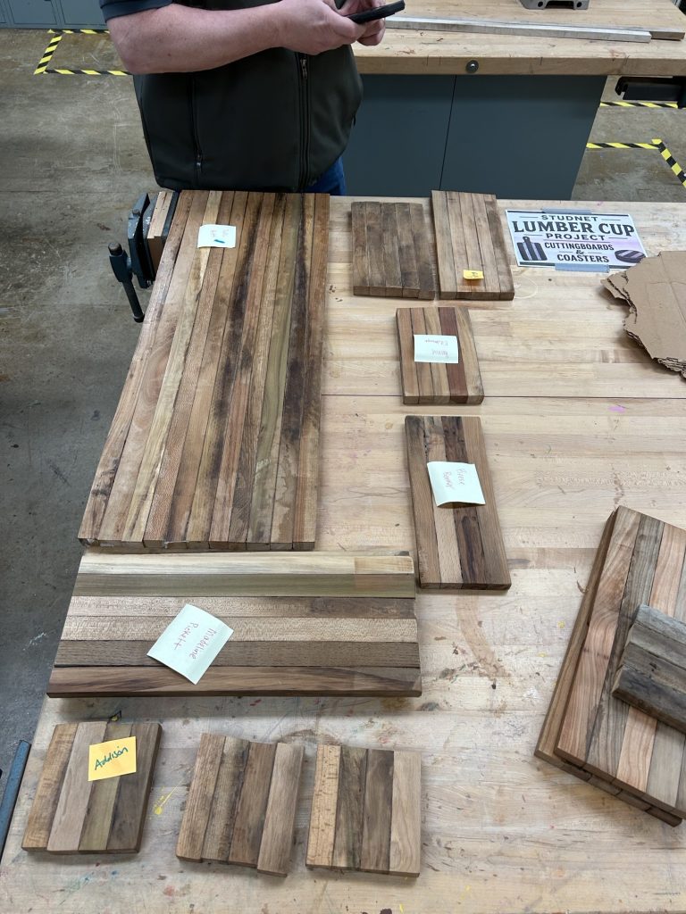 Workbench display with laminated spacer-stick cutting boards and coasters labeled by student names.