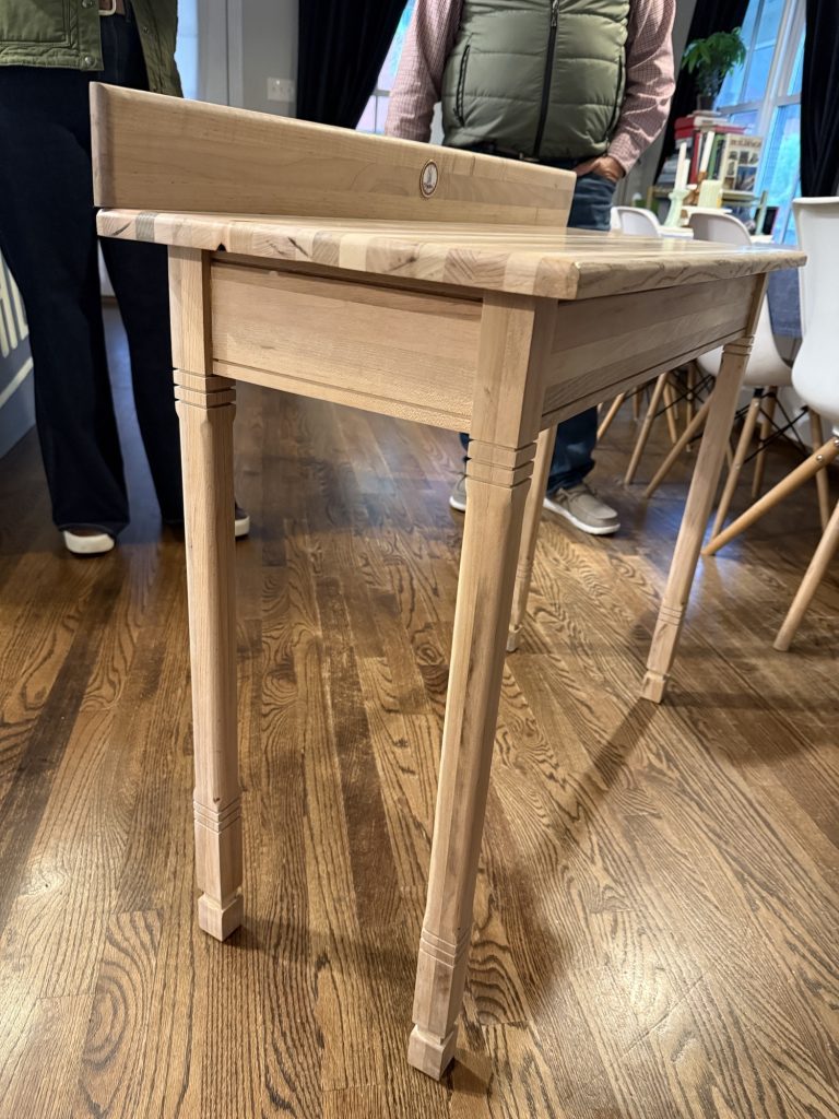Light-colored writing desk with a laminated spacer-stick top, back rail, apron, and decorative legs.