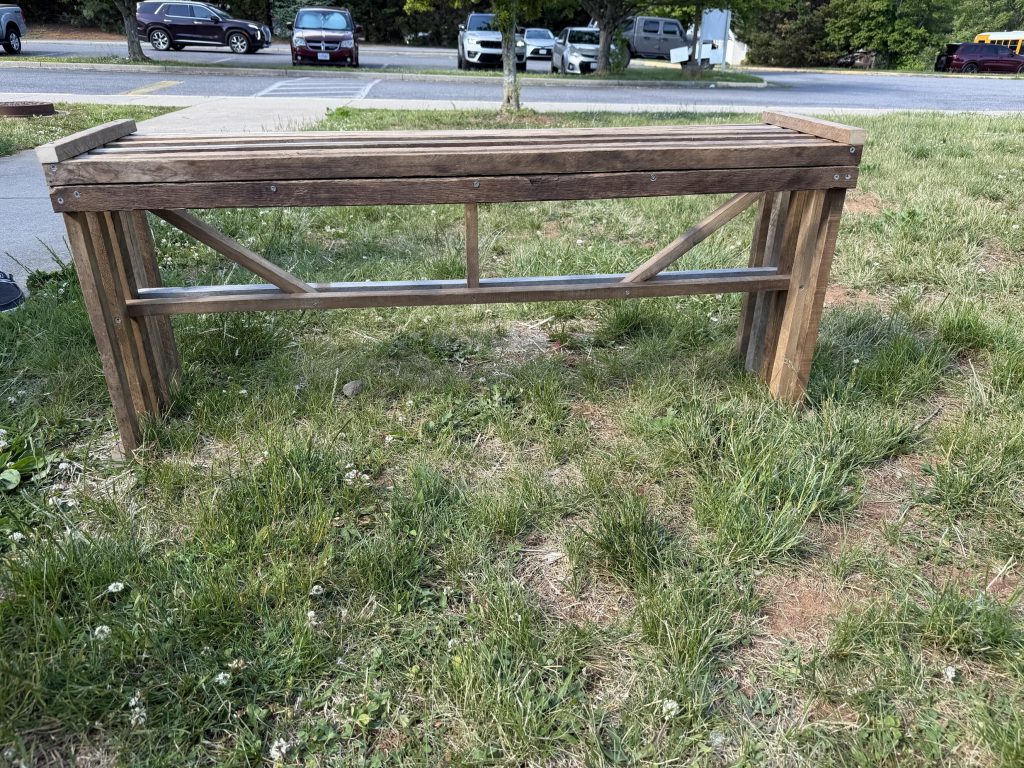 Long outdoor wooden bench with slatted top, straight legs, and diagonal side bracing.