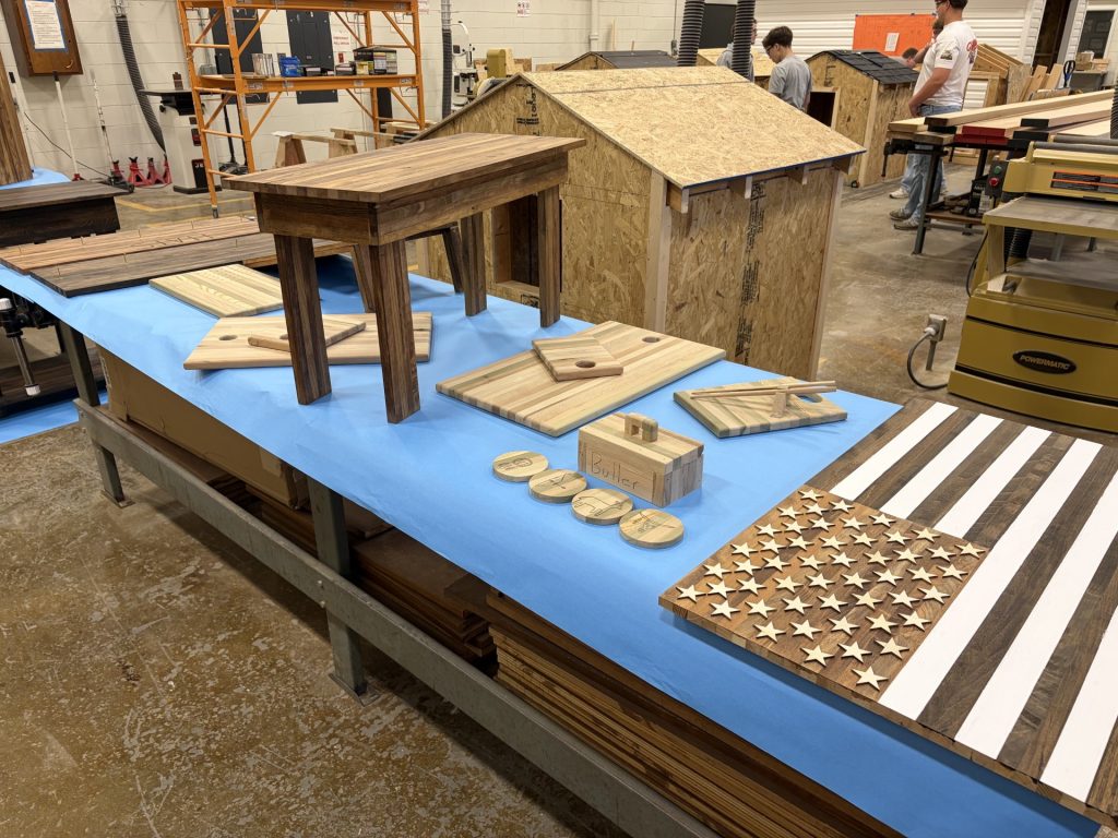 Display table with several spacer-stick projects including a side table, striped cutting boards, a small box, coasters, and a wooden American flag wall piece.