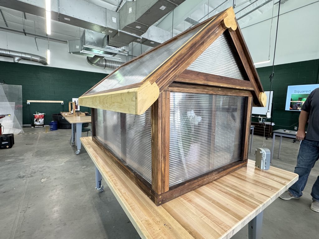 Greenhouse-style display with a spacer-stick wood frame, peaked roof, translucent panels, and contrasting wood trim.