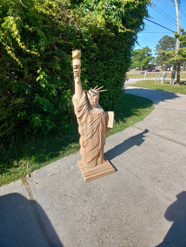 Carved wooden Statue of Liberty figure on a square wood base with robe, crown, torch, and tablet details.