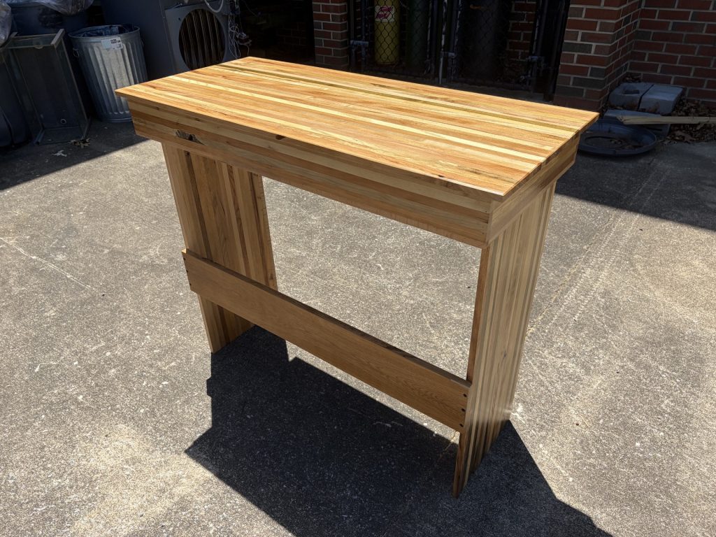 Tall spacer-stick table or stand with a laminated striped top, rectangular side panels, and sturdy cross supports.
