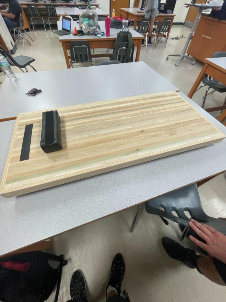 Laminated wooden mechanic's creeper on a classroom table with a striped surface, dark hardware, and a raised edge.